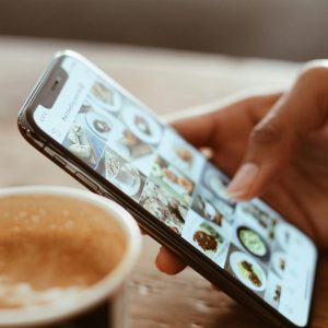 pexels-photo-1542252-1542252 Hand browsing social media photos on a smartphone next to a cup of coffee indoors.